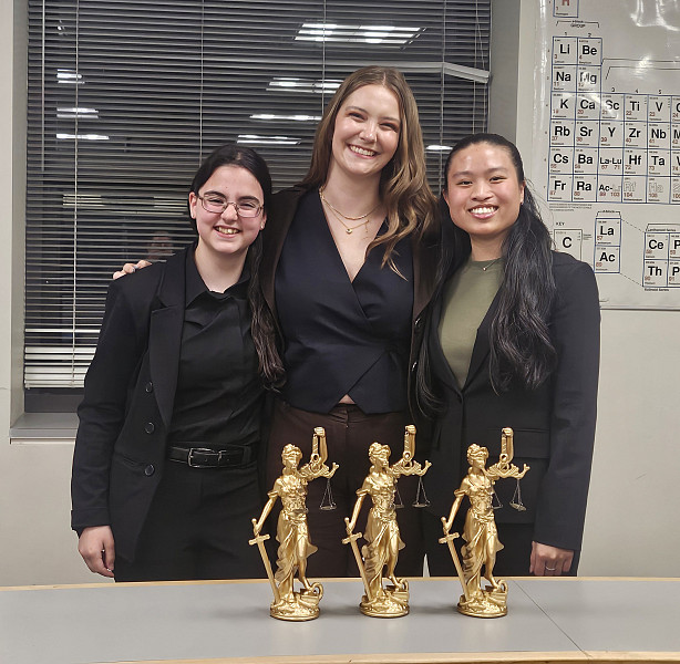 Pre-law legal writing students standing in front of gold trophies