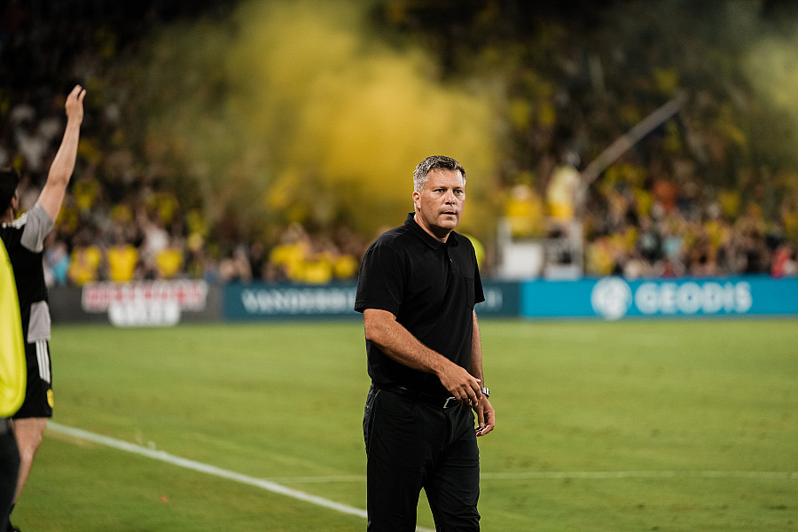 Nashville SC head coach B.J. Callaghan stands on the sideline in a black polo during a match.