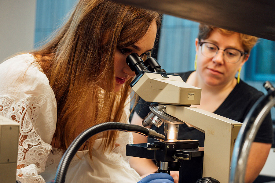 Students using a microscope in a lab as she is being supervised by a professor.
